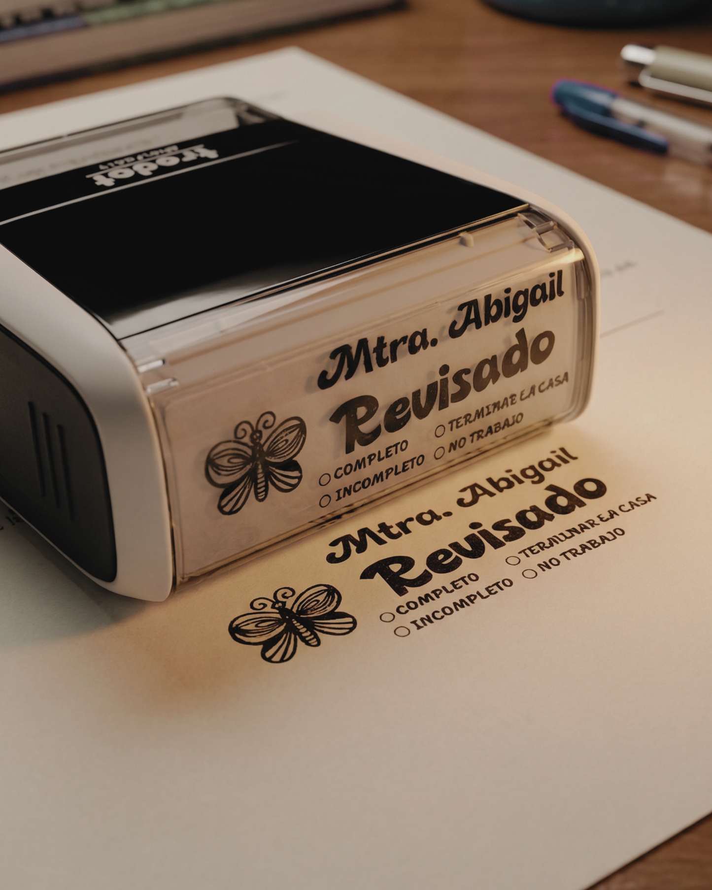 Sello personalizado para maestros con texto “Revisado” aplicado sobre hojas escolares.